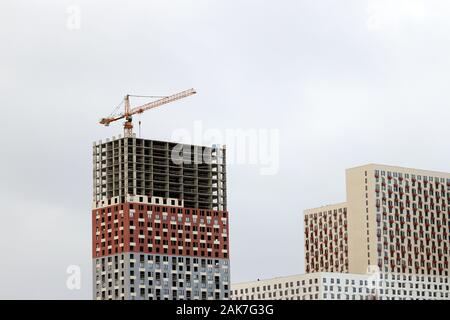 Gru da cantiere e edifici ad alta sullo sfondo del cielo nuvoloso. La costruzione di alloggi, appartamento blocco Foto Stock