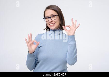 Caucasian donna matura con un ampio sorriso che indossano occhiali che mostra il simbolo ok con le dita. Il linguaggio del corpo okay significato super gesto per il negozio ottica, de Foto Stock