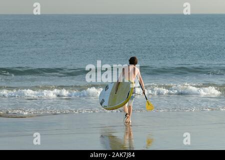 Durban, Sud Africa, persone singole giovane adulto uomo a camminare sulla spiaggia, SUP stand up paddle, sano esercizio, attività all'aperto, di un esercizio di stile di vita Foto Stock