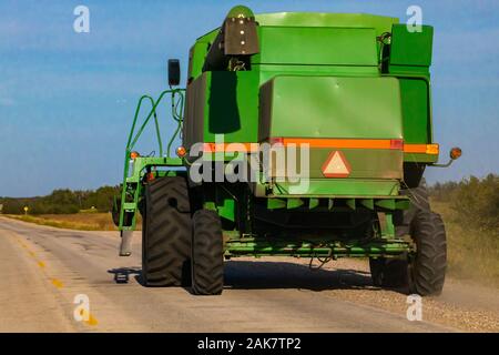 Un ampio e verde macchina mietitrebbiatrice è visto da dietro, parcheggiato su una strada di campagna. Il simbolo di attenzione e di nastro ad alta visibilità avvisa di veicolo lento Foto Stock