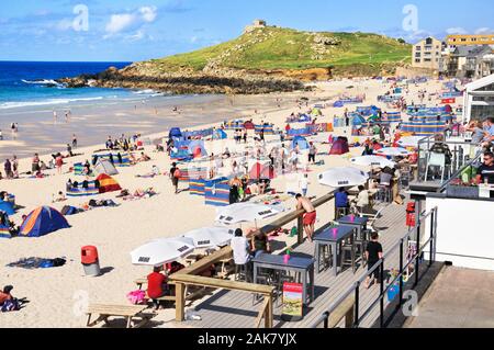I turisti per godersi il sole sulla spiaggia Porthmeor in alta estate presso la rinomata località balneare di St Ives in Cornovaglia, England, Regno Unito Foto Stock
