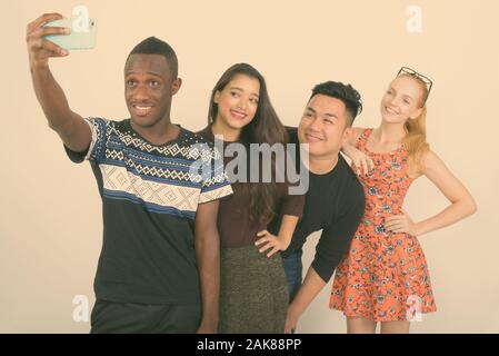 Studio shot di felice variegato gruppo di multi etnico amici sorridente e appoggiata sulla spalla mentre prendendo selfie foto con telefono cellulare insieme Foto Stock