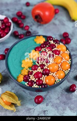 Yogurt sano e frullato di frutta ciotola con verde naturale spirulina in polvere e decorate con mirtilli rossi, physalis e kaki e quinoa soffiato Foto Stock