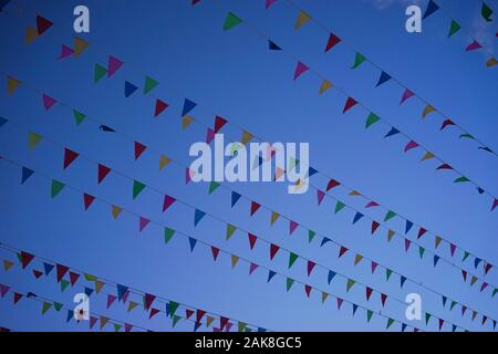 Una fila di decorazioni piccole bandiere svolazzanti nel vento contro lo sfondo di un profondo cielo blu. Foto Stock