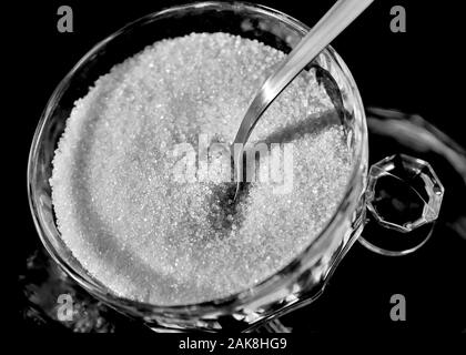 Ciotola di vetro di zucchero granulato con cucchiaio su sfondo nero Foto Stock