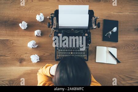 Vista dall'alto dello scrittore sopra la macchina da scrivere e le carte sbriciolate intorno. Concetto di problema di ispirazione Foto Stock