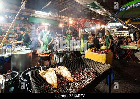 Bangkok, Tailandia - 28 dicembre 2019: persone cucinare grigliate di pesce e altri piatti in una bancarella di strada in Bangkok Chinatown intorno Yaowarat street in Tha Foto Stock