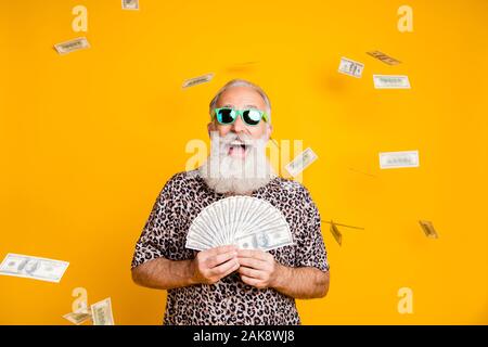 Foto di anziani vecchio fiducioso uomo ricco holding banconote nelle sue mani ed essendo piovuto con valuta mentre isolato con sfondo giallo Foto Stock