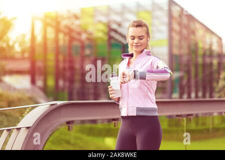 Donna Moderna ascoltando musica in cuffia mentre si verifica la frequenza cardiaca guardando smartwatch dopo fare jogging al mattino Foto Stock
