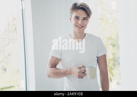 Ritratto di sua egli attraente bella carino allegro allegro ragazzo beve la mattina presto dolce cacao caldo a luce bianca in stile moderno hotel interni interni Foto Stock