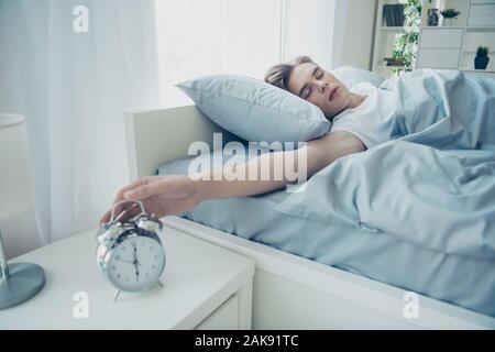 Ritratto di sognante stanco overslept capelli biondi uomo disteso sul letto per avere una giornata difficile ieri ignorando la campana che squilla in casa al chiuso Foto Stock