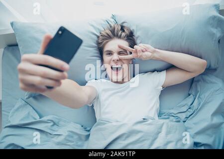 Parte superiore in alto sopra la foto angolo positivo di capelli biondi uomo hanno weekend divertente sdraiato sul letto in camera da letto casa blogging prendere selfie rendere v-segni interni Foto Stock