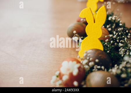 Elegante uova di pasqua, giallo bunny nel nido di fiori di primavera sulla tavola in legno rustico, spazio per il testo. Tinto naturale uova di Pasqua e il coniglio di decorazioni su Foto Stock