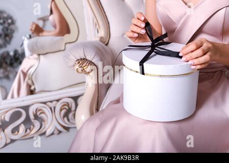 Donna con le mani in mano nel vestire tenendo un round confezione regalo con nastro nero. Regalo di compleanno box. Regalo di natale Scatola vintage. Mani di una confezione regalo Foto Stock