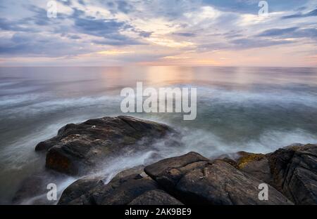 Scenic Sunset Over Water visto dalla spiaggia rocciosa, tempo di esposizione lungo, lo Sri Lanka West Coast. Foto Stock