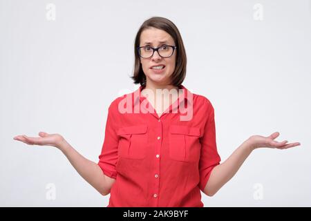 Si chiedeva la donna in bicchieri e maglietta rossa isolato sul muro bianco. Non so che cosa scegliere. Studio shot Foto Stock