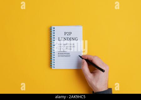 Maschio di scrittura a mano un P2P modello di prestito delle priorità nella sua spirale notepad decidere se investire o meno. Su sfondo giallo. Foto Stock