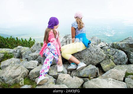 Due ragazze seduto e riposo dopo le escursioni sul picco di montagna guardando a valle verde in dei monti Tatra. Foto Stock