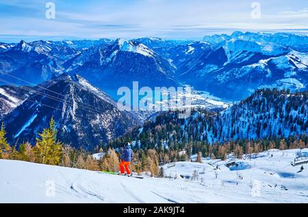 L'inverno il paesaggio alpino con uno sciatore, rendendo in discesa lungo la Feuerkogel pendio di montagna con una vista sulla città di Ebensee nel lago Traunsee valley, Salzk Foto Stock