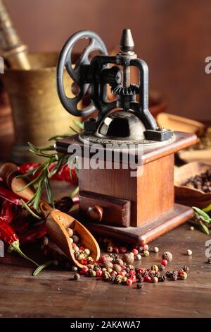 Vecchio mulino di pepe con utensili da cucina, spezie e rosmarino su un tavolo di legno. Foto Stock