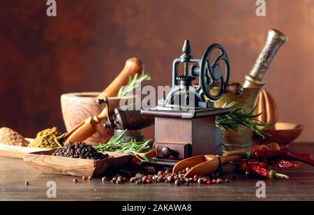Vecchio mulino di pepe con utensili da cucina, spezie e rosmarino su un tavolo di legno. Foto Stock