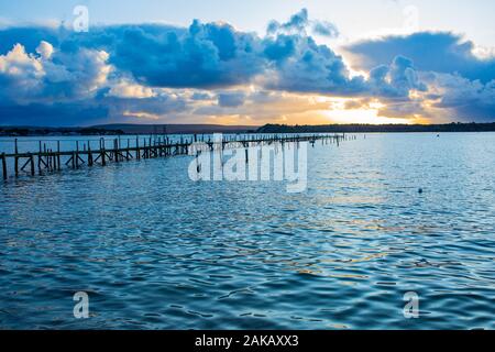 Foto a colori del paesaggio che si affaccia sull'acqua del porto di Poole con un piccolo molo in legno antico sullo sfondo durante il tramonto, preso a Poole, Dorset Foto Stock
