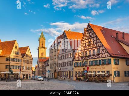 Dinkelsbuhl, Germania - 11 Maggio 2019: alberghi e negozi lungo la Marktplatz (piazza del mercato) con la Chiesa di San Paolo in background Foto Stock