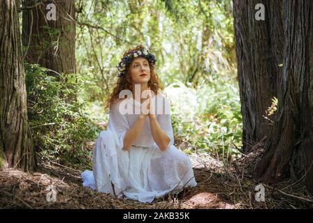 Donna con fiore seduto con le mani incrociate in foresta, Bainbridge Island, nello Stato di Washington, USA Foto Stock