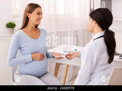 Gravidanza e cure mediche. Terapeuta dando una donna incinta medicine prescritte pillole seduto in un ufficio moderno. Messa a fuoco selettiva Foto Stock