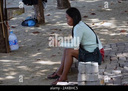 Pattaya, Thailandia - 24 dicembre 2019: Donna seduta su piastrelle pavimentate vicino alla spiaggia e guardare il suo telefono. Foto Stock