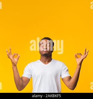 Mantenere la calma. Zen-Like Afro Guy meditando in piedi su sfondo giallo. Studio Shot, spazio di copia Foto Stock