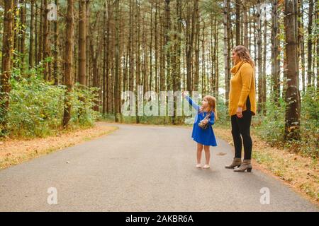 Un bambino piccolo si alza su un sentiero boscoso con la madre che punta in su Foto Stock