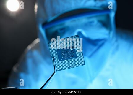 Mano maschio in blu guanti protettivi con le pinzette tenere micro rocessore Foto Stock