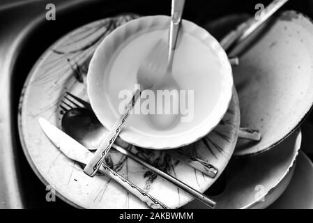 Un bianco e nero di sporco piatti, ciotole e posate in lavello da cucina in attesa di lavaggio fino. Foto Stock