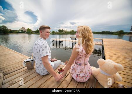 Data romantica sorpresa. Un ragazzo e una ragazza su un molo in legno. Il ragazzo versa dello Champagne nei bicchieri Foto Stock