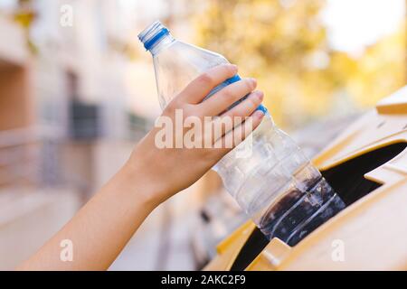 Stock Foto di una donna di riciclaggio a mano una bottiglia di plastica in un contenitore giallo per salvare l'ambiente Foto Stock