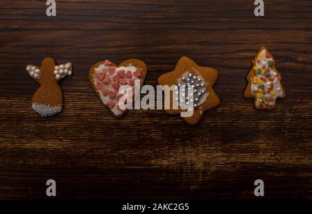 pan di zenzero fatto in casa di varie forme con glassa bianca e decorazione colorata dello zucchero sullo sfondo di un vecchio tavolo di legno Foto Stock