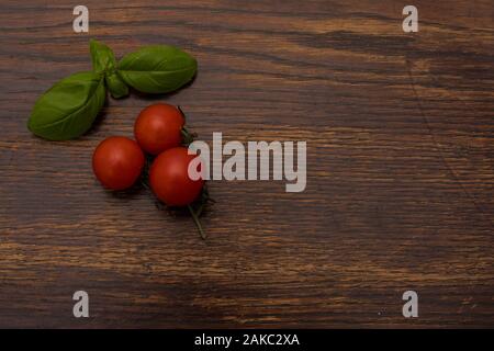 Close-up di basilico foglie e tre rossi pomodori ciliegia sulla vecchia sullo sfondo di legno Foto Stock
