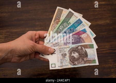 Close up di varie banconote denaro polacco, zloty, PLN tenuto in una forma a ventaglio in mani su un vecchio sfondo di legno Foto Stock
