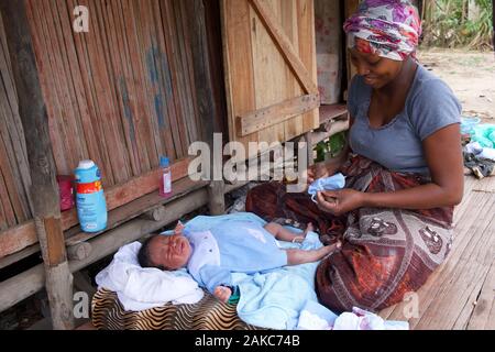 Madagascar, Diana regione, villaggio di Marosely, una donna abiti il suo bambino di fronte alla sua casa Foto Stock