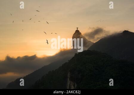 Tramonto a Rio de Janeiro - Fregate in cielo con silhouette di Cristo Redentore in aumento dalla nebbia in background Foto Stock