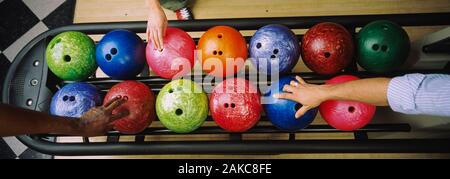 Tre popoli mani scegliendo le palle da bowling Foto Stock