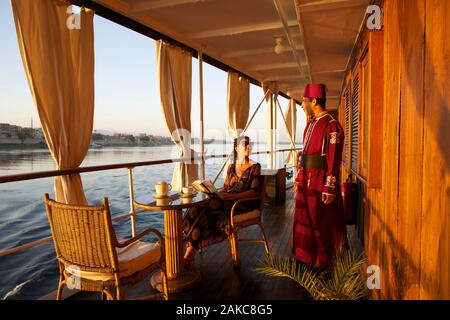 Egitto Alto Egitto, Valle del Nilo, turistico seduto in un passaggio della nave a vapore il Sudan, l'ultimo steamboat crociera sul Nilo, al fianco di un membro di equipaggio in costume e indossando un cappello. tarbouche Foto Stock