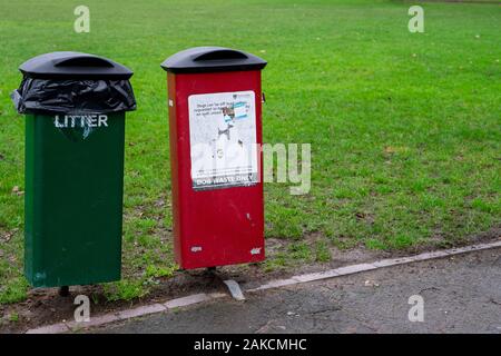 Un cestino verde vicino ad un cestino del cane rosso in un parco Foto Stock