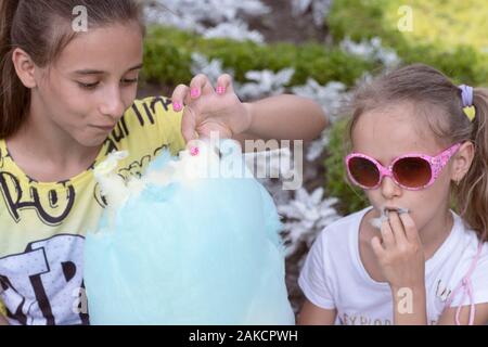 Due ragazze in natura mangiare caramella di cotone. Infanzia felice momenti. Soleggiata giornata estiva.adorabili poco sorelle mangiando caramelle-filo interdentale all'aperto in estate. Foto Stock