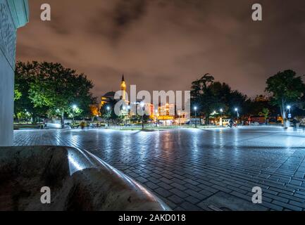 A tarda notte vista da Piazza Sultanahmet come turisti passano da vicino un minareto illuminato e moschea di Istanbul, Turchia Foto Stock