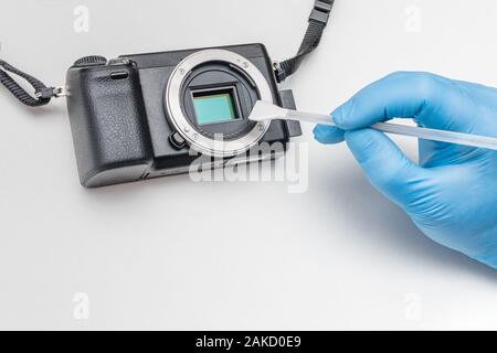 Pulizia della fotocamera digitale matrice. Fotocamera digitale servizio. Il master in guanti pulisce la matrice della telecamera digitale dalla contaminazione con una scopa a frange Foto Stock