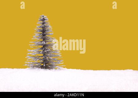 Toy argento albero di Natale artificiale sul bianco della neve contro sfondo giallo Foto Stock