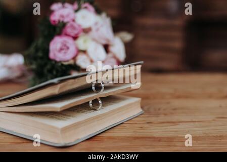 Due anelli di nozze in un libro e un mazzo di nozze sulla tabella. Foto Stock