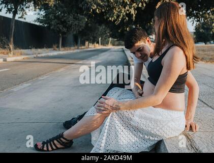 Attraente giovani incinte caucasico giovane seduto sul cordolo Foto Stock